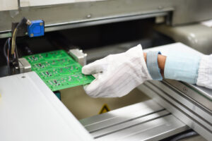 Electronic manufacturing factory workers hand covered with ESD gears removing printing circuit board from SMT line. It illustrates how experienced PCB engineers transform schematics into robust PCB designs.